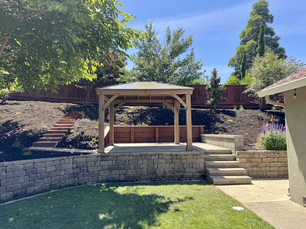 Finished Walnut Creek backyard: a raised paver patio with a wood gazebo, wood retaining wall and stone steps set into a replanted hillside